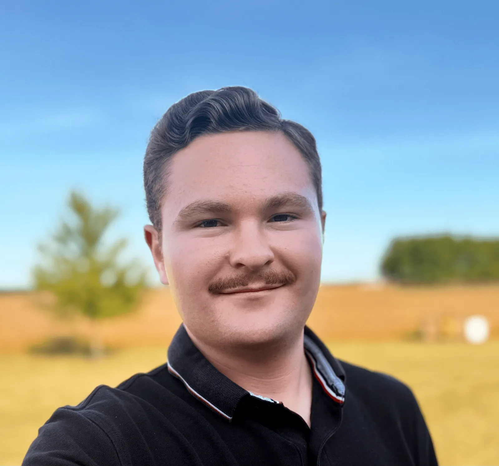 Smiling man outdoors in front of a field and trees